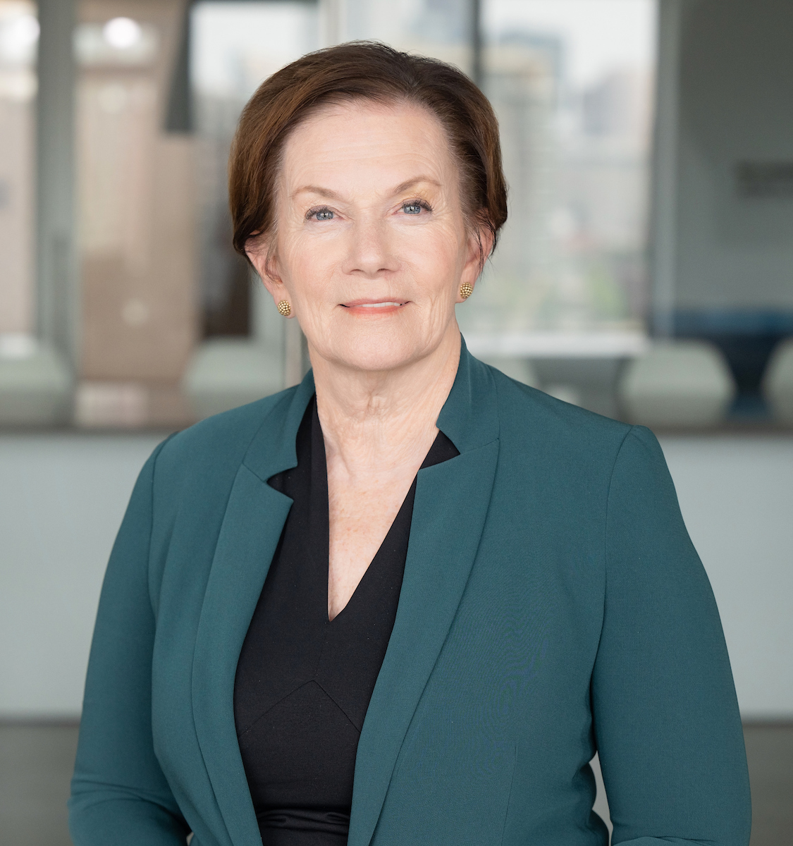 Donna Lynne, DrPH, chief executive officer of Denver Health, poses for a professional headshot in a teal blazer and black top, with a softly blurred office background behind her.